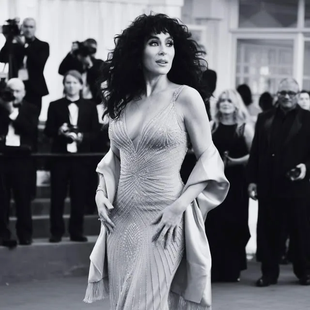 A woman in an elegant dress posing on a red carpet, surrounded by photographers.